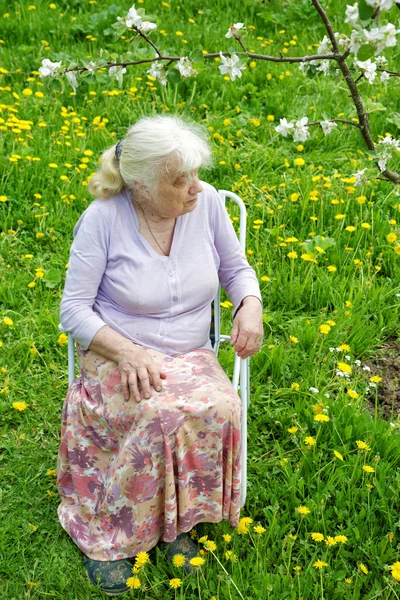 Bahçede çiçek açan elma ağacının altındaki büyükanne.