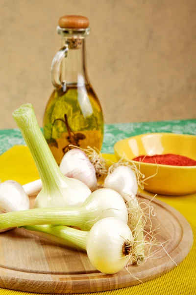 Cipolla e aglio con una bottiglia di olio d'oliva su un tavolo da cucina — Foto Stock