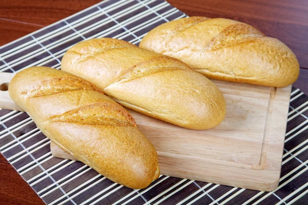 Três longos loafs em uma tábua de corte — Fotografia de Stock