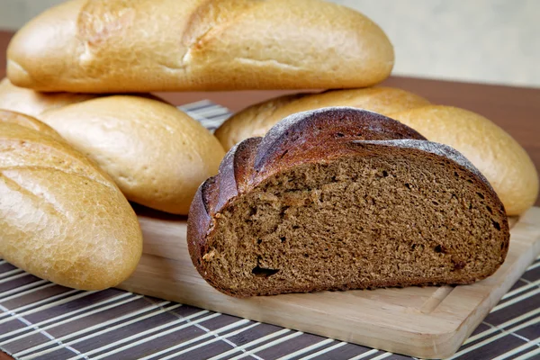 Черный хлеб и белые булочки на кухонном столе — стоковое фото