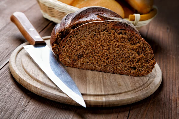 Řez černého chleba na dřevěný stůl — Stock fotografie