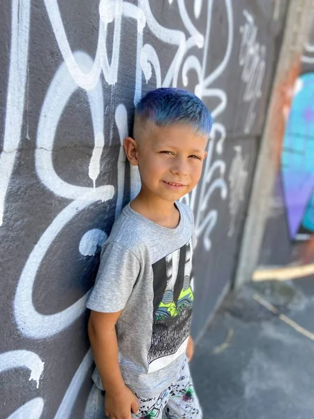 落書きのある色の壁の背景に明るい青の髪のかわいい面白い男の子 — ストック写真