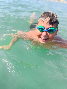 Kafkasyalı çocuk dalgıç maskesi takıyor. Büyük bir gülümsemeyle denizde yüzüyor.