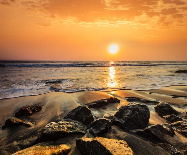 Vågor och klippor på solnedgångens strand — Stockfoto