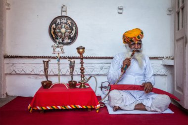 Old Indian man smokes hookah (waterpipe) in Mehrangarh fort clipart