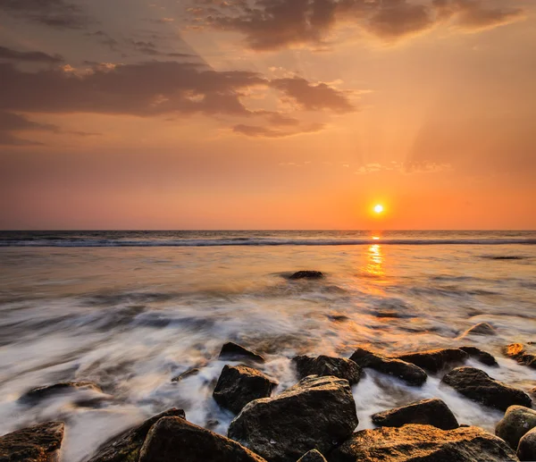 Vågor och klippor på solnedgångens strand — Stockfoto