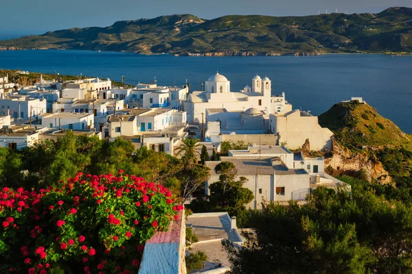 Picturesque scenic view of Greek town Plaka on Milos island over red geranium flowers — Stock Photo, Image