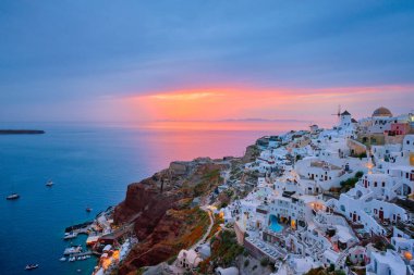 Yunanistan 'ın başkenti Santorini' de geleneksel beyaz evleri ve yel değirmenleriyle Yunanistan 'ın başkenti Alacakaranlık' ta gün batımında ünlü ikonik selfie noktası turizm beldesi Oia köyü