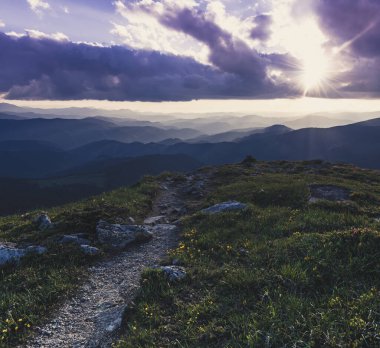 Bulutlu gökyüzünde renkli günbatımına ve kayaların arasındaki yola sahip inanılmaz dağ manzarası, doğal arka plan yolculuğu. Güzellik dünyası.