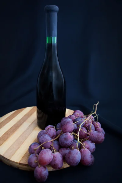 Бутылка вина и винограда на доске — стоковое фото