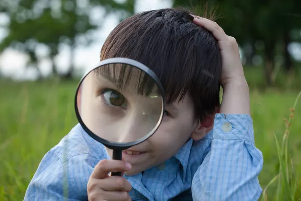 Jongen met Vergrootglas liggen op het gras — Stockfoto