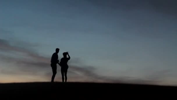 Relaxado jovem casal pasionado desfrutando da beleza do pôr do sol em sua lua de mel, em um deserto com fundo laranja — Vídeo de Stock