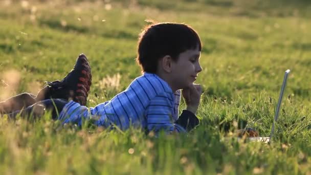 Pojken med sin laptop utomhus i parken på gräs — Stockvideo