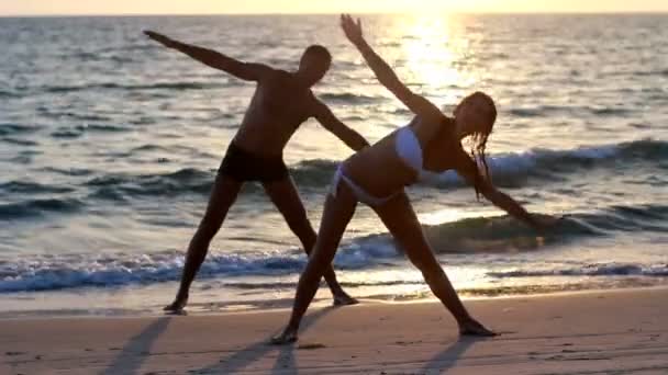 一个有魅力的年轻女人和男人做瑜伽上一个突堤码头与海洋 — 图库视频影像