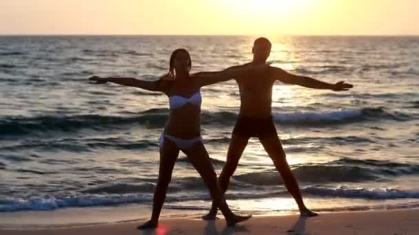 Una atractiva joven y hombre haciendo yoga en un embarcadero con el océano — Vídeos de Stock