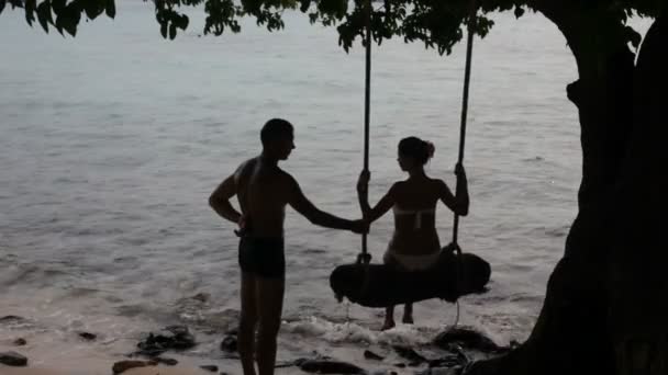 Mann stößt Frau auf Schaukel glückliches Paar am Meer im Urlaub. — Stockvideo