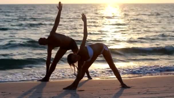 一个有魅力的年轻女人和男人做瑜伽上一个突堤码头与海洋 — 图库视频影像
