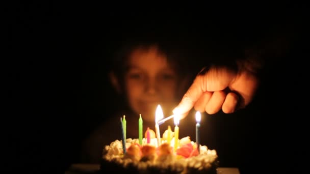 Older boy lights candles on younger boy's birthday cake. younger boy cheers. — Stock Video