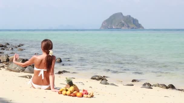 Femeia tânără se relaxează pe plajă și mănâncă fructe — Videoclip de stoc