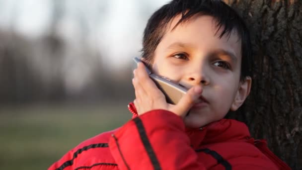 Мальчик разговаривает по мобильному телефону на улице — стоковое видео