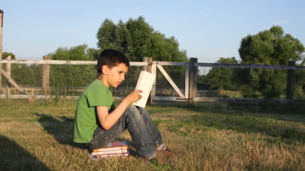 Garçon lit livre en plein air — Video