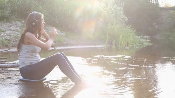 Girl with headphones by lake — Stock Video