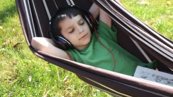 Niño leyendo y escuchando música en hamaca — Vídeos de Stock