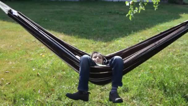 Boy reading and listening to music in hammock — Stock Video