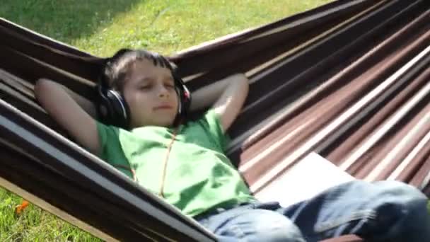 Niño leyendo y escuchando música en hamaca — Vídeos de Stock