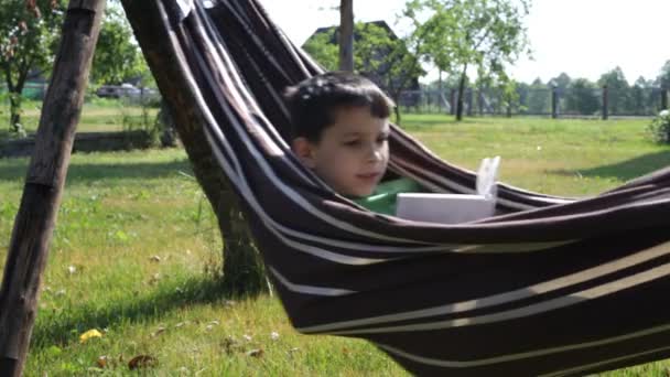 Мальчик читает книгу в гамаке — стоковое видео