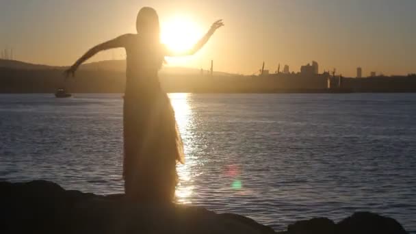 Mutlu bir kadın deniz arka plan ile gün batımında sahilde dans — Stok video