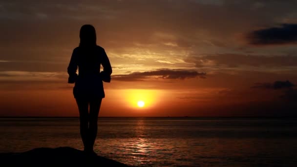 Жінка танцює на пляжі на заході сонця з морським фоном — стокове відео