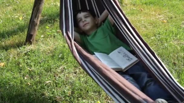 Niño leyendo un libro en hamaca — Vídeo de stock
