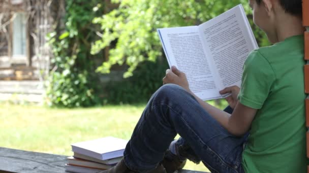 Хлопчик читає книгу на відкритому повітрі — стокове відео