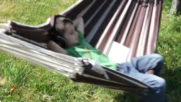 Chłopiec czytanie i słuchanie muzyki w hamaku — Wideo stockowe