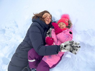 Annesiyle birlikte karda yatan küçük bir kız ve ikisi de gülümsüyor. Kış eğlencesi konsepti.
