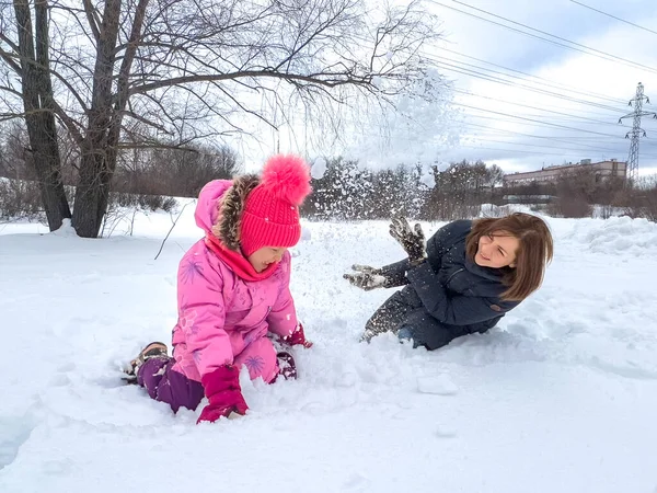 小さな女の子と彼女の母親が雪の中で遊んでいて 彼らは両方とも笑っています 冬の楽しみの概念 — ストック写真