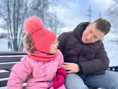 Baba ve küçük kızı parkta bir bankta sohbet ediyorlar. Kış yürüyüşü konsepti.