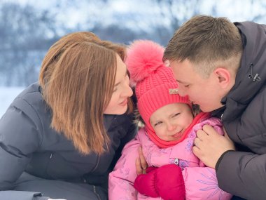 Anne ve baba parkta yürürken kızlarını öpüyor. Aile kavramı..
