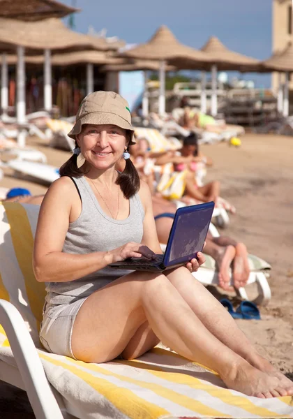Mature woman with laptop at resort beach — Stock Photo, Image