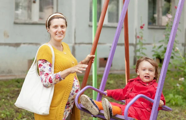 Pregnant woman with child on swing in autumn park — Stock Photo, Image