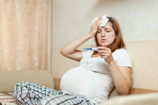 Беременная женщина с термометром дома — стоковое фото