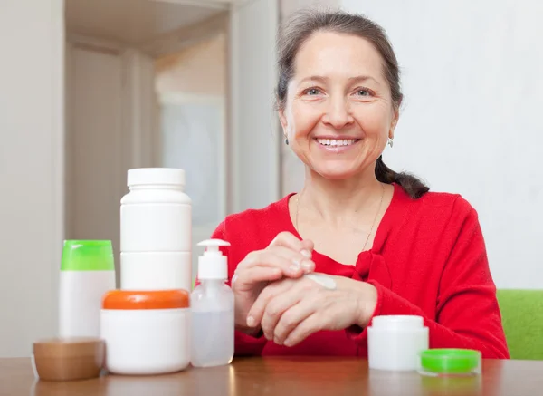 Mature woman in red dress applying cream on hands — Stock Photo, Image