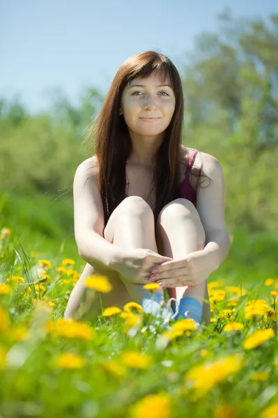 Meisje zit in paardebloem weide — Stockfoto