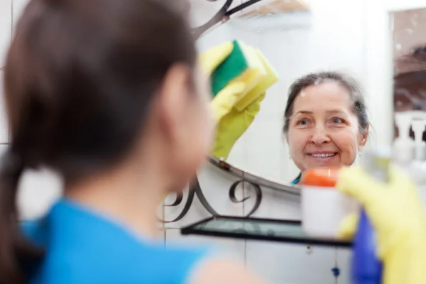 Mogen kvinna rensar spegel med svamp — Stockfoto
