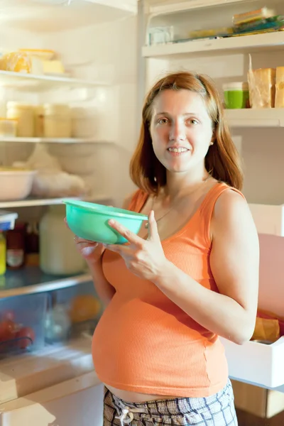 Mujer embarazada con plato cerca del refrigerador —  Fotos de Stock