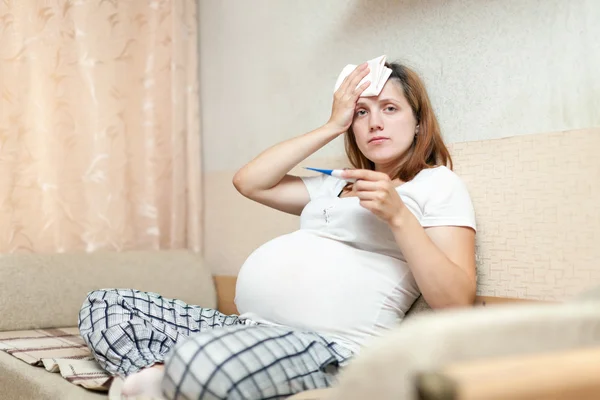 Těhotná žena s teploměrem v obývacím pokoji — Stock fotografie