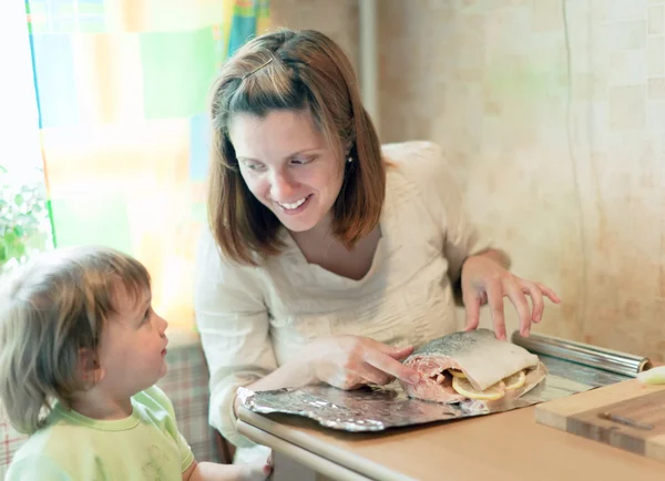 Happy mother with girl foiling salmon — Stock Photo, Image