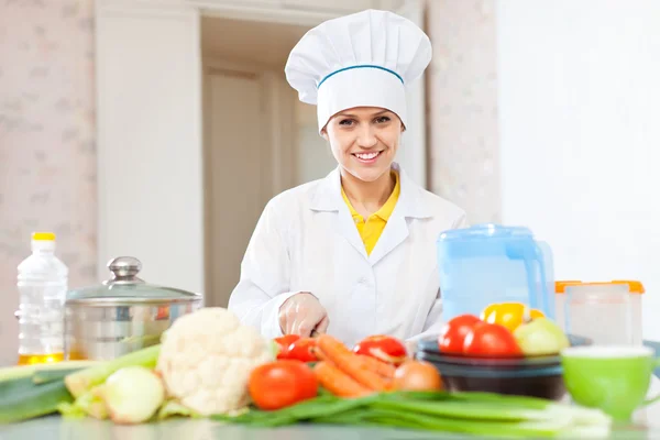 Koken vrouw in uniforme snijden groenten — Stockfoto