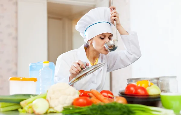 Cook in white uniform tests soup from ladle — Stock Photo, Image